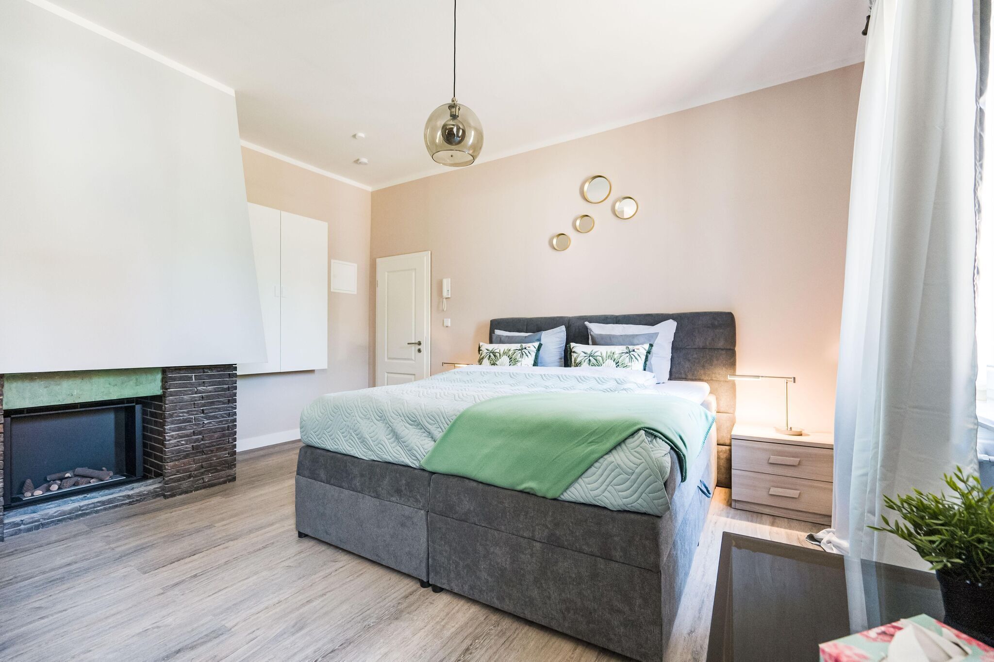 A bedroom with a bed, a nightstand, a lamp, a fireplace, and a wall-mounted mirror.