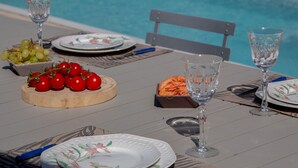 Una mesa de comedor servida con platos, vasos y una tabla de madera con tomates y uvas.