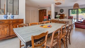 Un comedor amplio con una gran mesa y sillas de madera, una cocina con armarios de madera, y vistas a través de ventanas grandes.