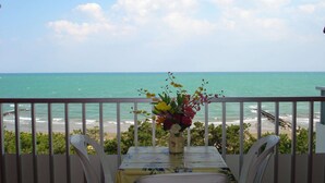 Un balcon avec une table et des chaises donnant sur une plage et l’océan.
