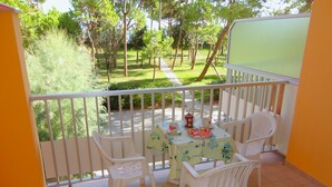 A balcony with a table and chairs, a view of a garden, and a green screen.