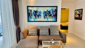 A modern living room with a sectional sofa, a glass coffee table, and a painting on the wall. - B12a - 2 Bdr Serviced Apt with Pool Access, Karon Beach (Tambon Karon)