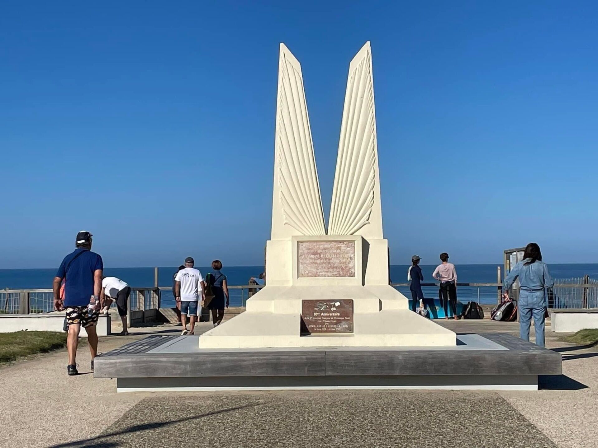 Een monument met twee grote vleugels, omgeven door een verharde looppad met mensen die lopen.