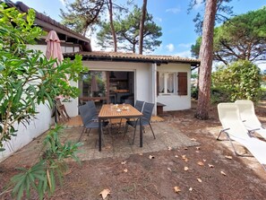 A small house with a patio, a table with chairs, and a white chair outside. - Cosy apartment for 6 people with WIFI, TV, terrace and pets allowed (Mimizan)