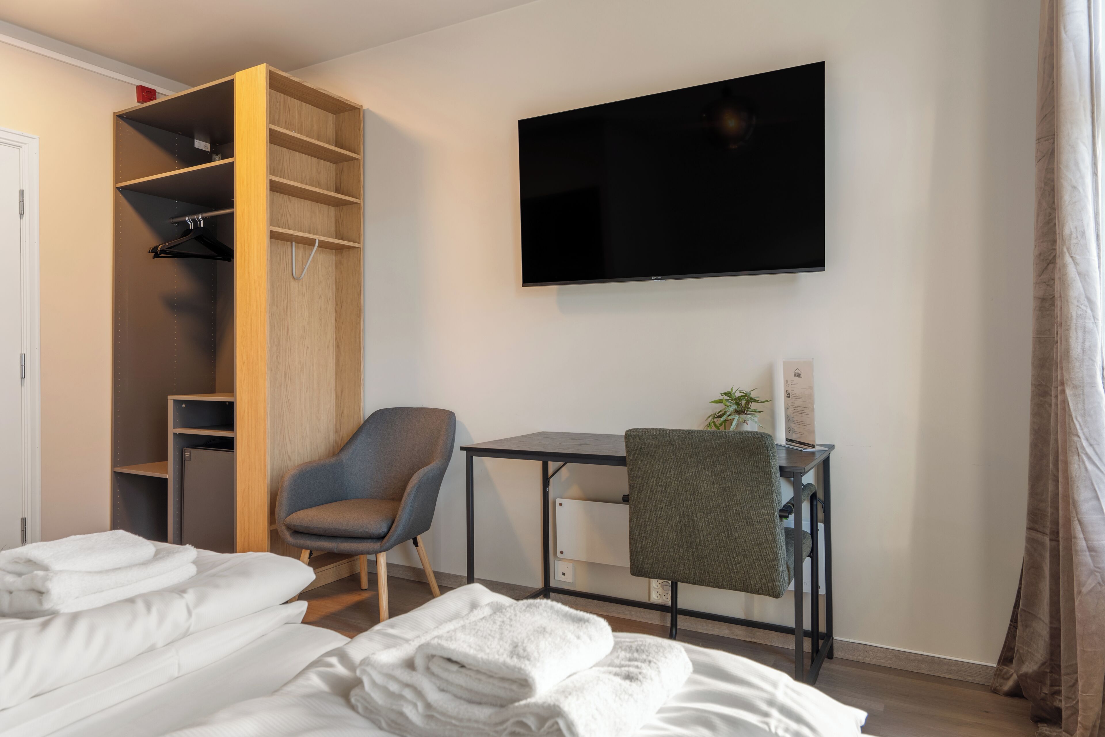 A hotel room with a bed, a desk, a chair, a TV, and a wardrobe.
