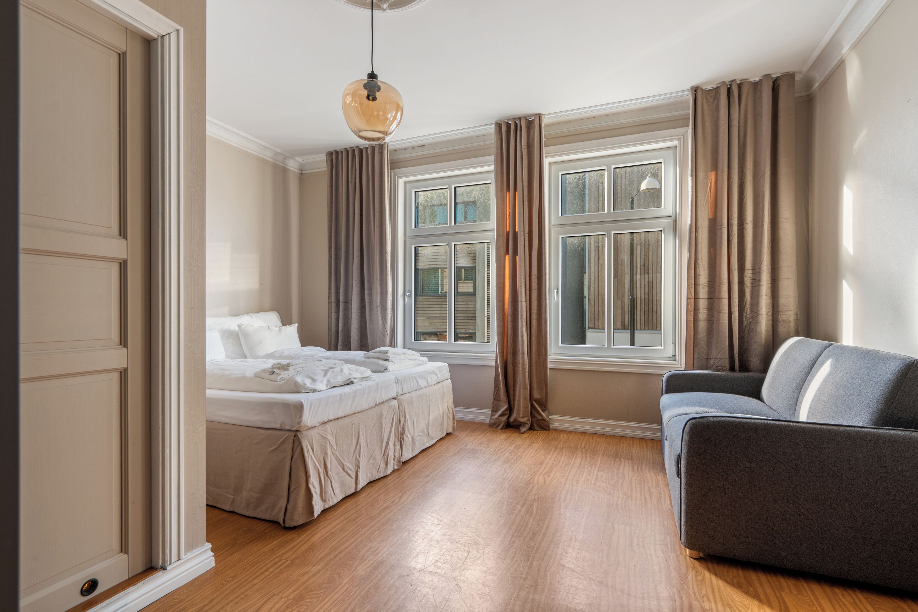 Un dormitorio con cama, sofá, ventana con cortinas y lámpara colgante.