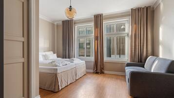 Un dormitorio con cama, sofá, ventana con cortinas y lámpara colgante.