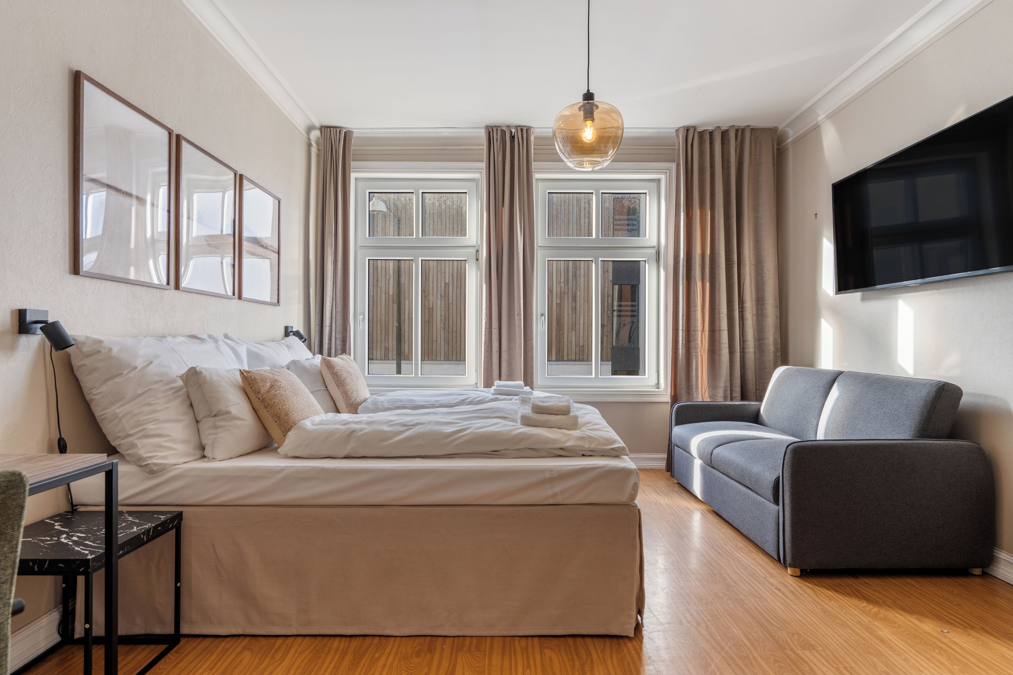 Una habitación de hotel con cama, sofá, televisor y ventana con cortinas.
