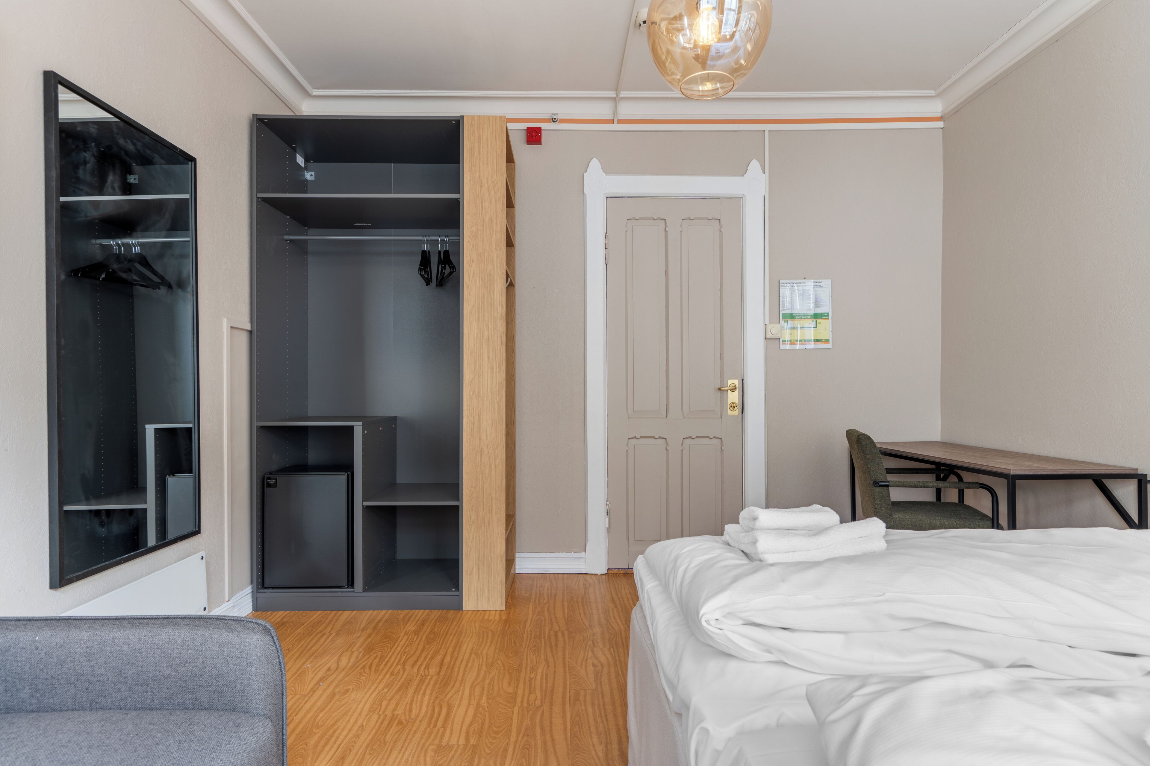 Une chambre d’hôtel comprenant un lit, un bureau, une chaise, une armoire et un miroir.