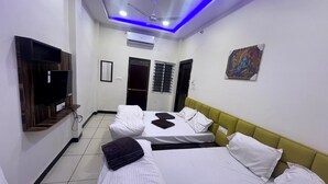 Camera d'albergo con due letti, televisore, condizionatore e ventilatore a soffitto.