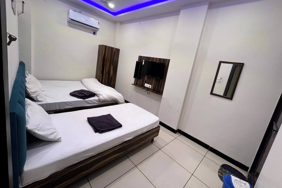 A hotel room with two beds, a TV, a mirror, and an air conditioning unit.