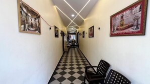 Un corridoio con pavimento a scacchi, quadri appesi alle pareti e una fila di sedie in fondo.