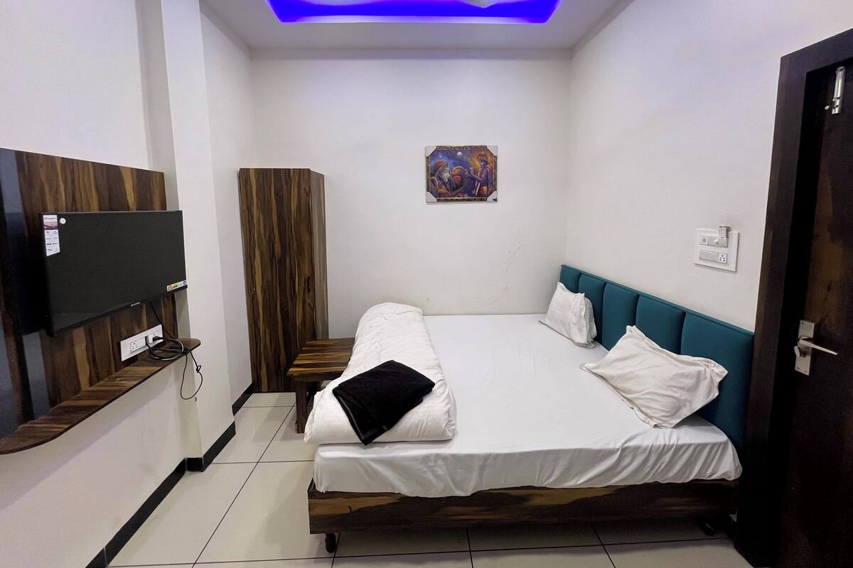 A bedroom with a bed, a TV mounted on the wall, a ceiling light, and a door.