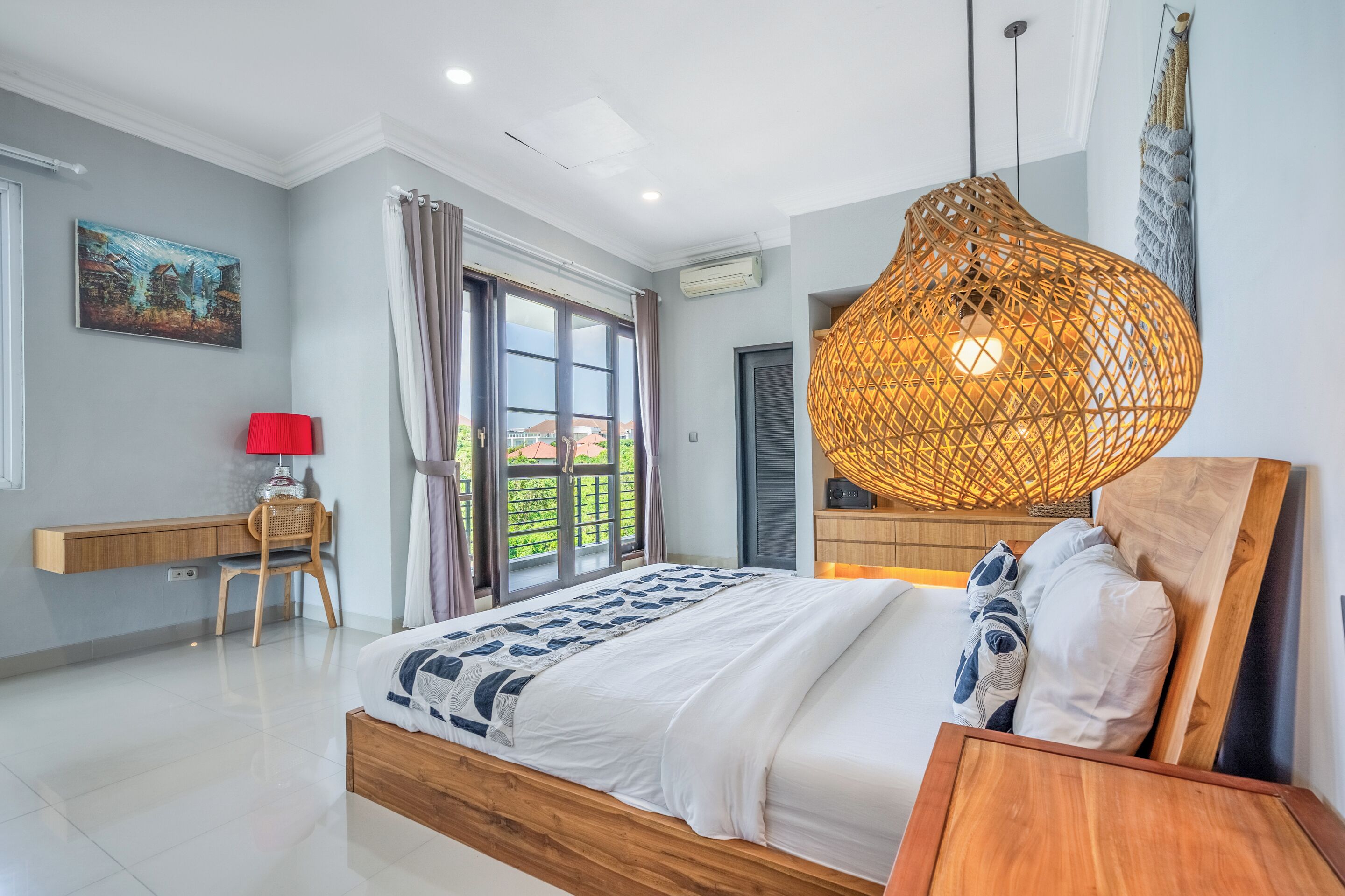 A bedroom with a bed, a desk, a chair, a hanging light fixture, and a window with curtains.