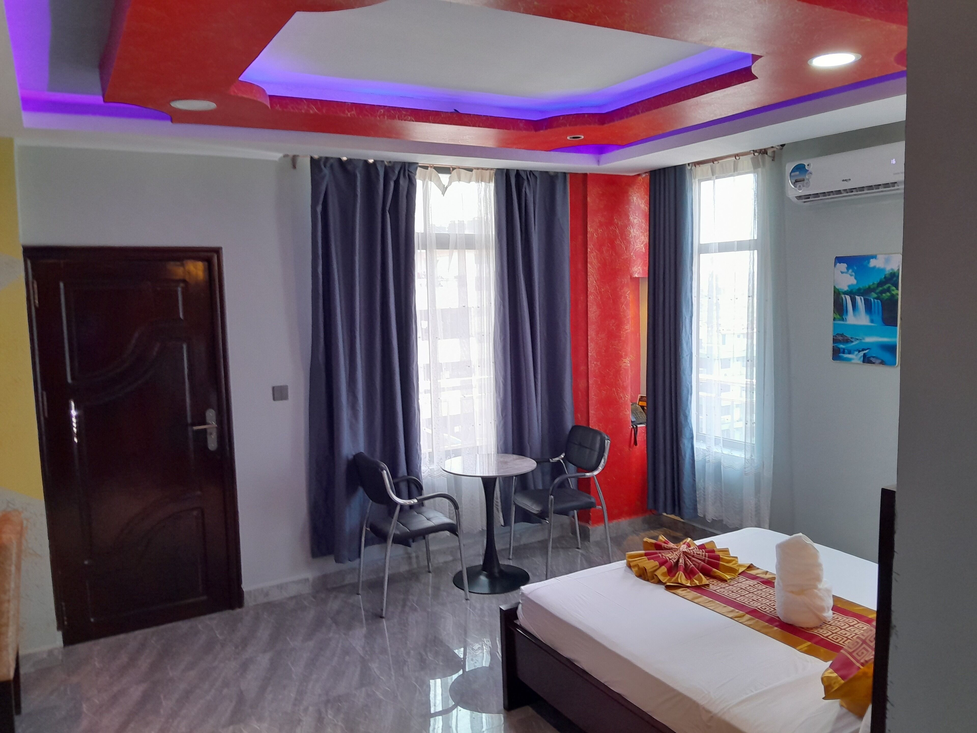 A hotel room with a bed, two chairs, a small table, a door, and a window with curtains.