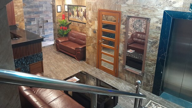 A lobby with a reception desk, leather sofas, a staircase, and a marble wall with artwork. - MAZOLA DIAMOND HOTEL (Dar es Salaam)
