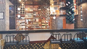 A bar area with shelves of various liquor bottles, a counter, and several chairs with a patterned upholstery. - MAZOLA DIAMOND HOTEL (Dar es Salaam)