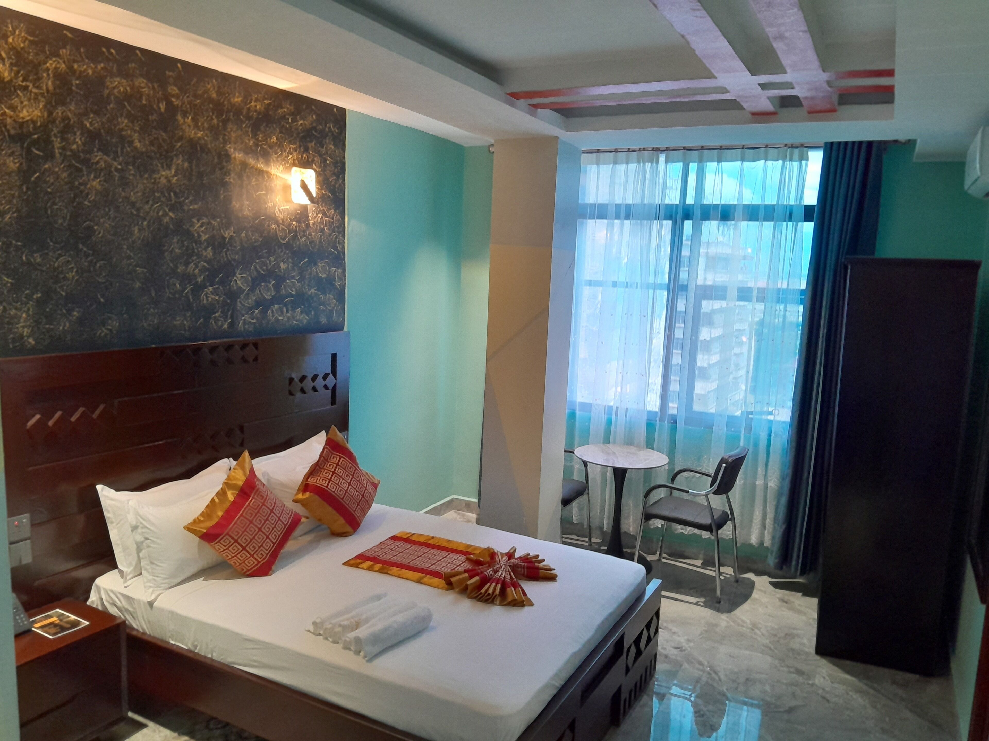 A hotel room with a bed, bedside table, and a small table with chairs near a window.