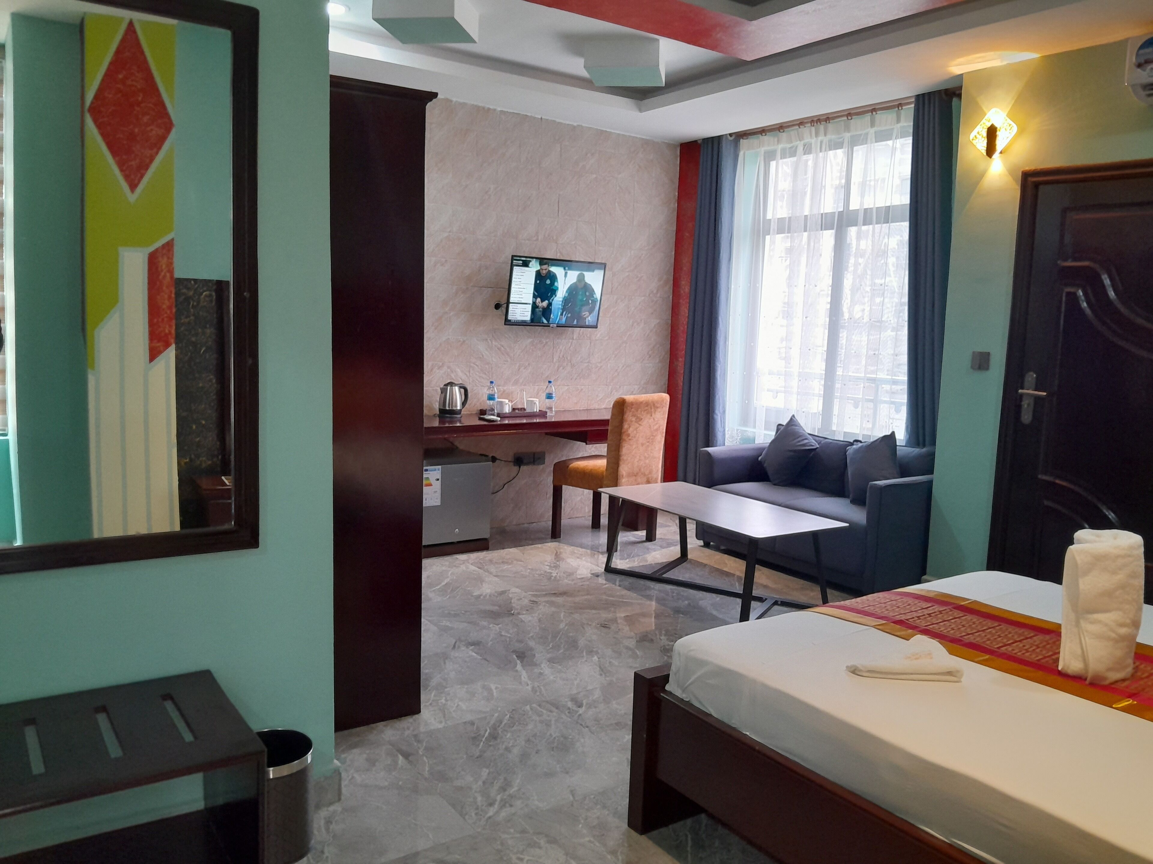 A hotel room with a bed, a desk, a chair, a sofa, a TV, and a window with curtains.