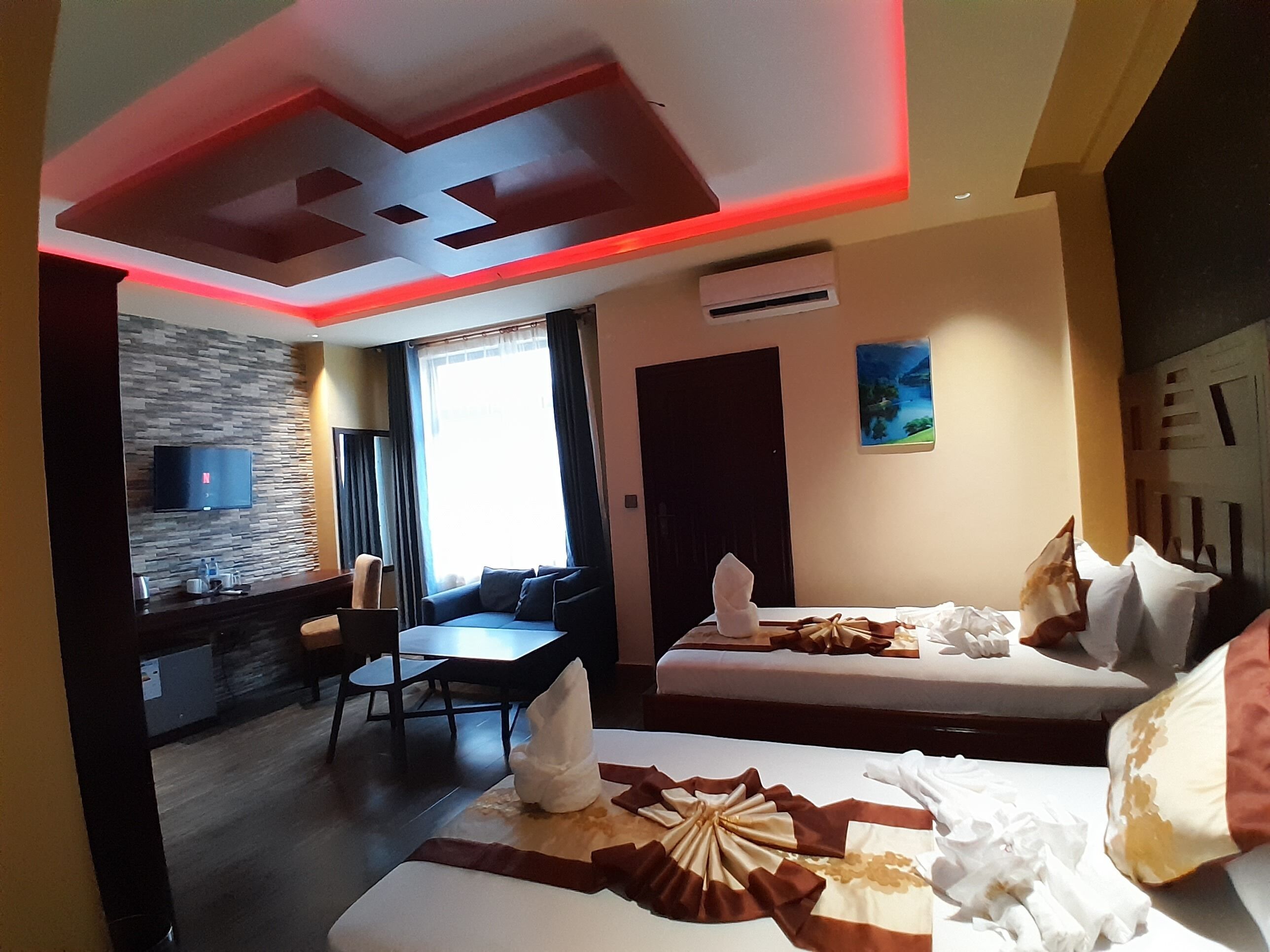 A hotel room with two beds, a dining area, a TV, and a painting on the wall.