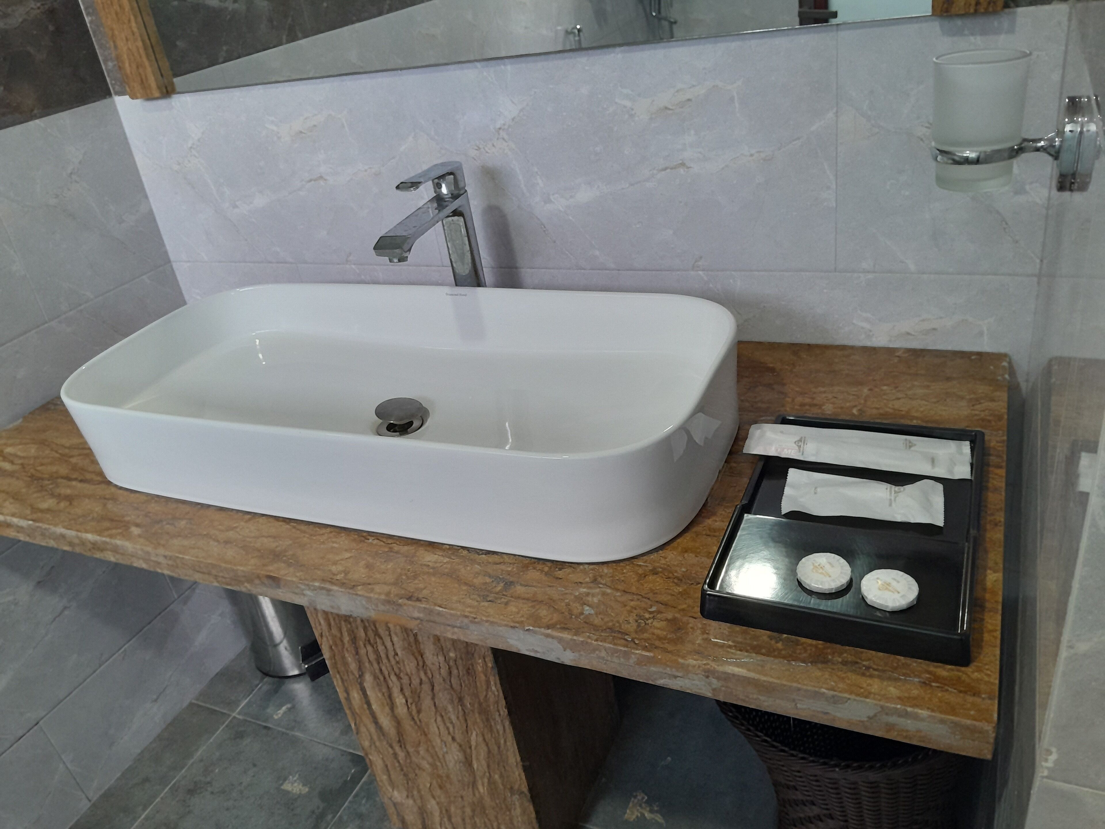 A bathroom with a white rectangular sink, a wooden countertop, and a small tray with two white objects.