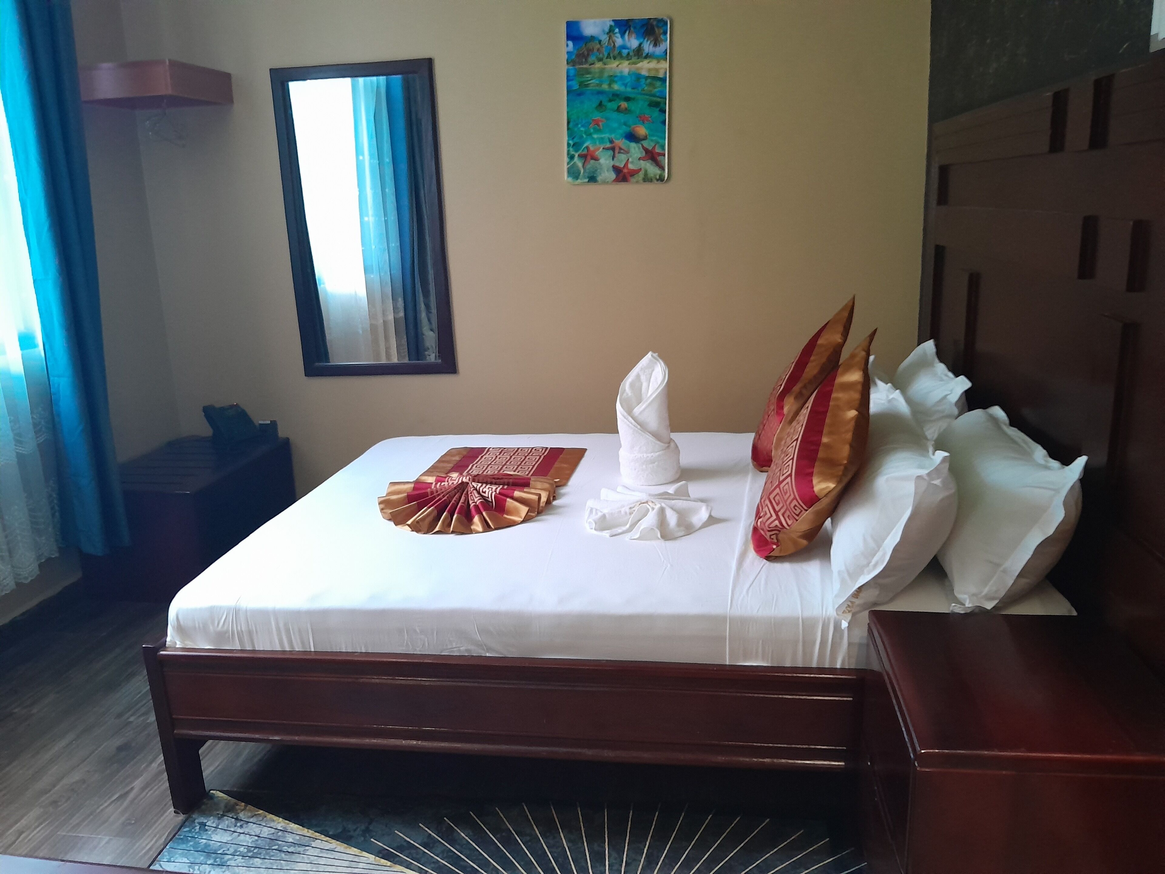 Un lit bien fait, avec un couvre-lit blanc et des coussins décoratifs, une tête de lit en bois, une petite table de chevet et un tableau accroché au mur.