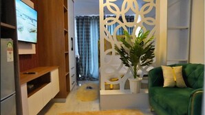 A living room with a green sofa, a TV on the left, and a decorative partition with a plant. - Smart Homes - Elysian Escape (Nairobi)