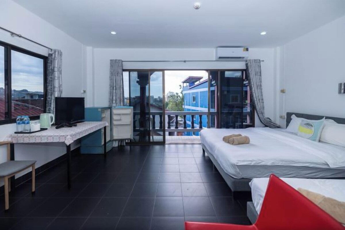 Habitación de hotel con cama, escritorio, televisión y balcón con vistas a edificios.
