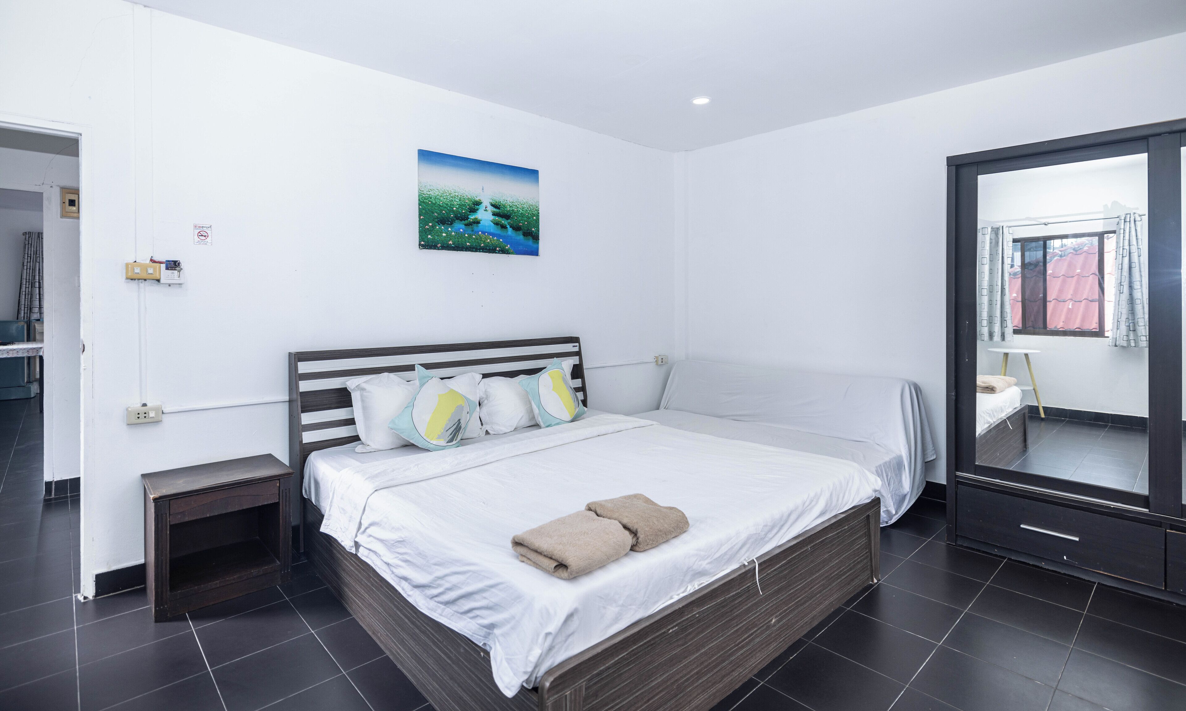 Ein modernes Schlafzimmer mit einem großen Bett, einem Nachttisch, einem kleinen Beistelltisch, einem Wandbild und einem großen Spiegel.