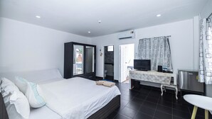 Habitación de hotel con cama, escritorio con televisor, refrigerador y baño visible a través de una puerta abierta.
