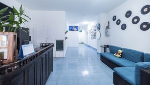 Un vestíbulo de hotel con una mesa de recepción, un sofá azul con un oso de peluche y discos de vinilo colocados en la pared.