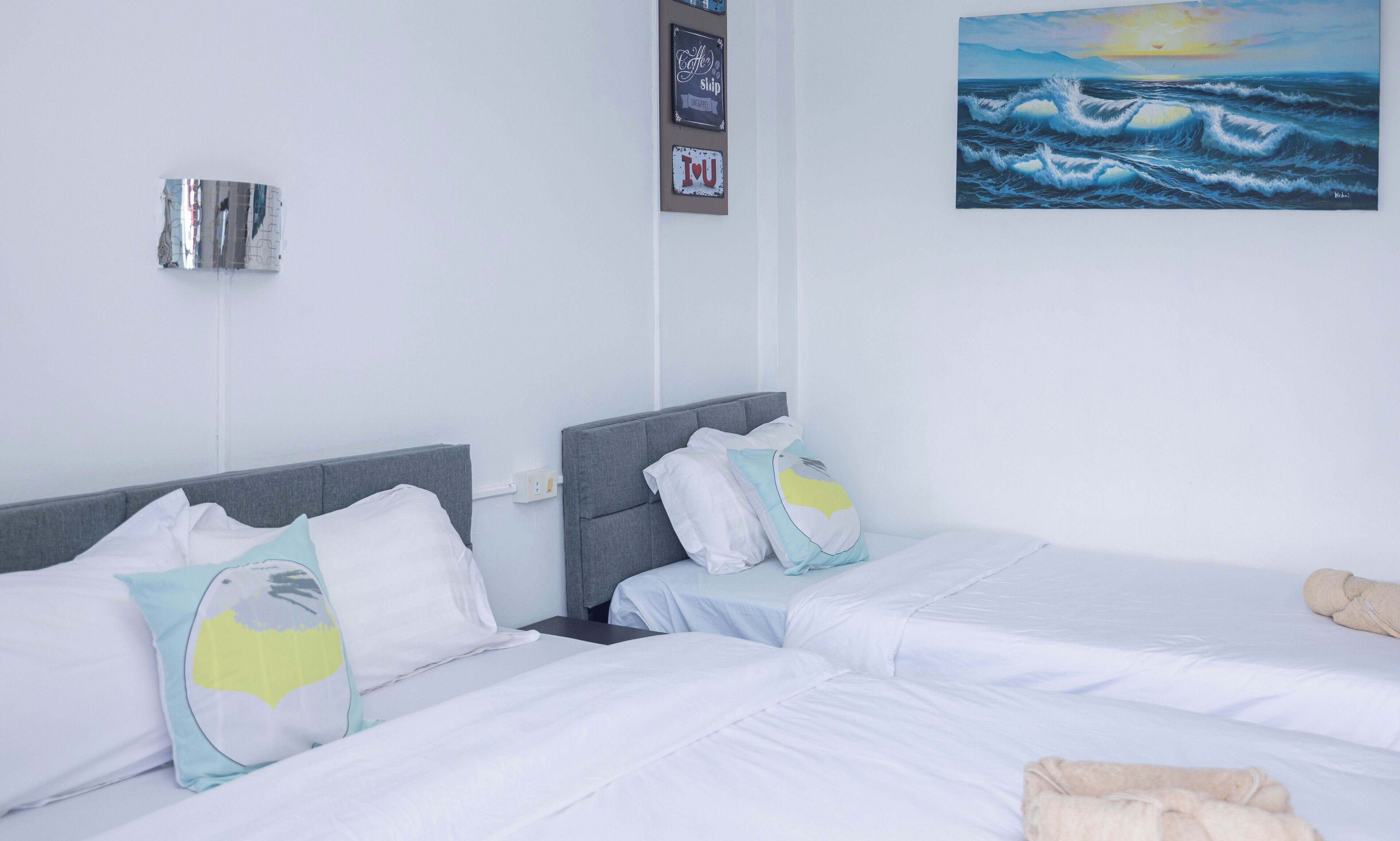 A hotel room with two beds, white bedding, and a painting of a seascape.