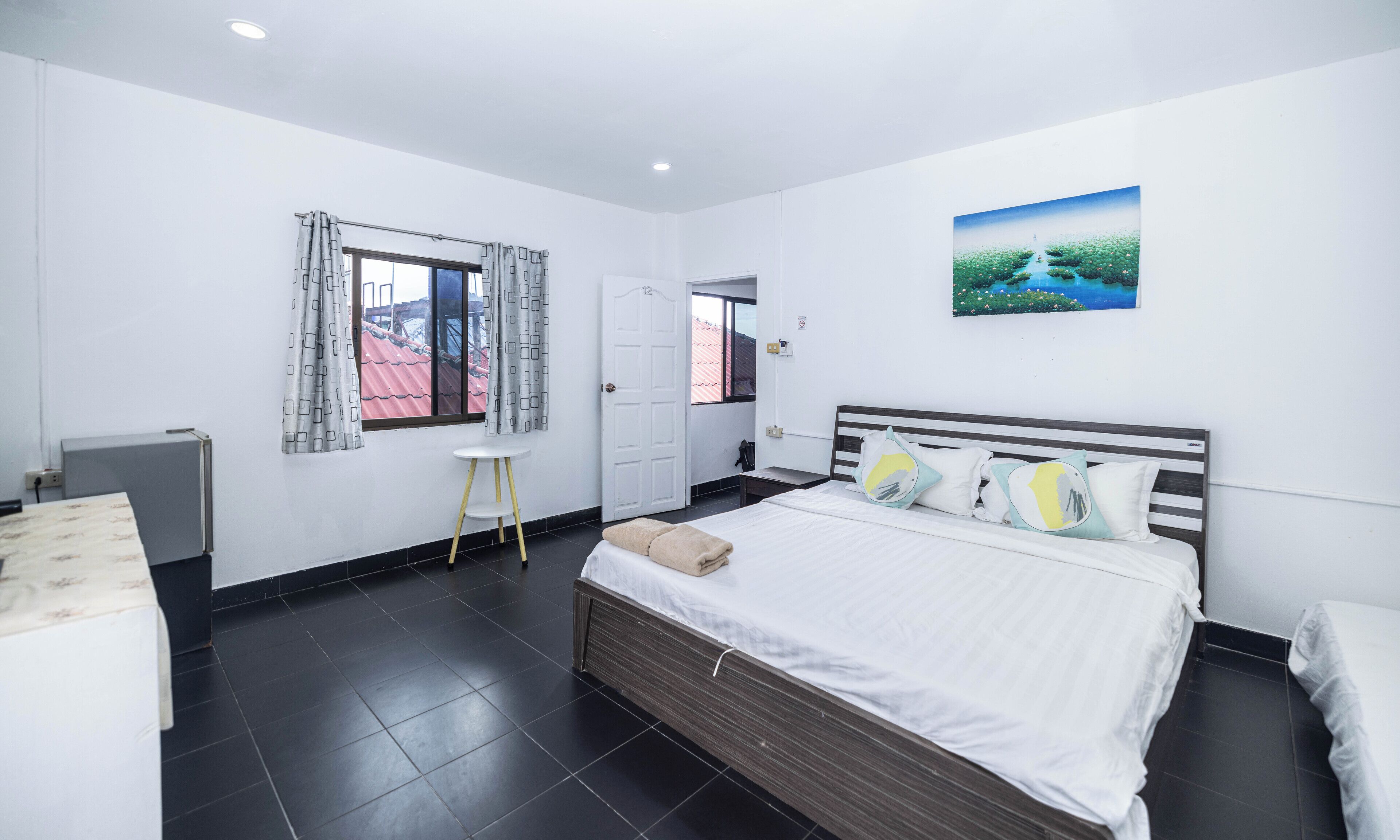Une chambre à coucher avec un lit, une table de chevet, une fenêtre avec des rideaux, une porte et un tableau au mur.