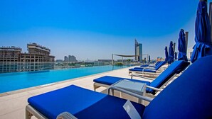 A rooftop pool area with blue lounge chairs and umbrellas, overlooking a cityscape. - GLOBALSTAY. Avani Palm View (Dubai)