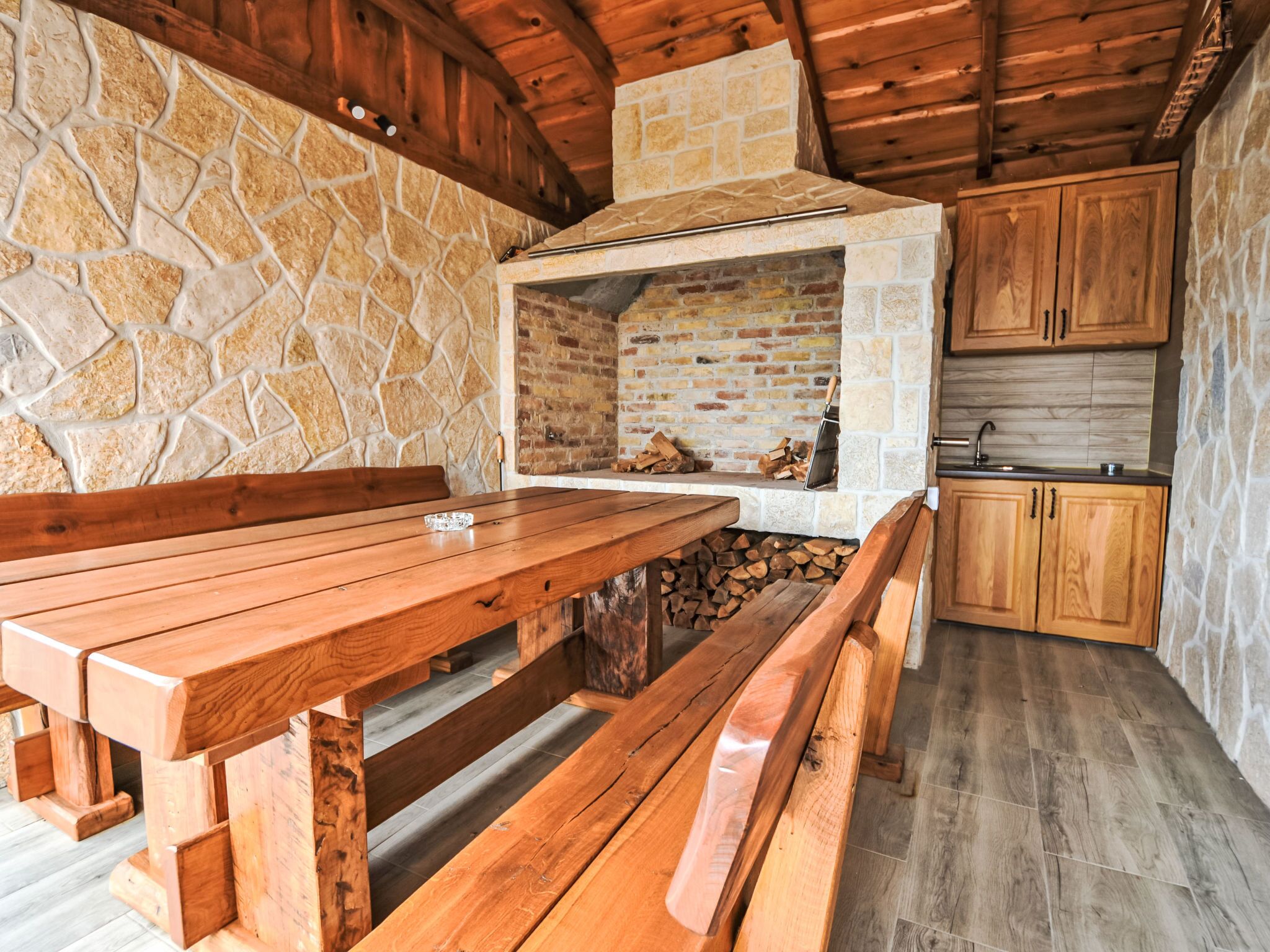 Eine rustikale Außenküche mit Steinwand, Holzbänken und Backofen aus Ziegeln.