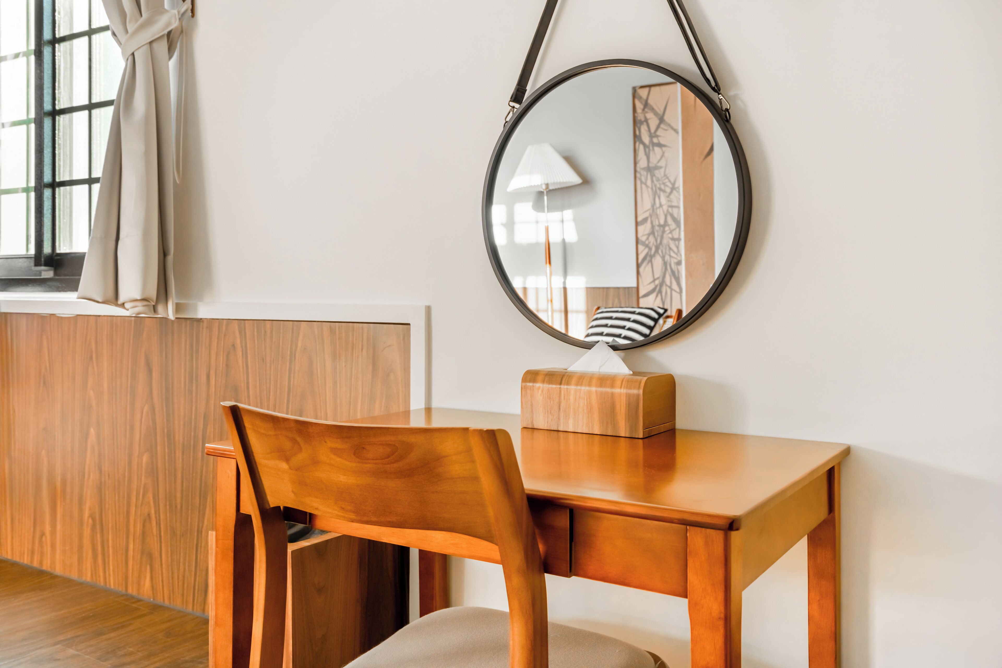 Un bureau en bois, agrémenté d’un miroir rond, d’une boîte de mouchoirs et d’un coussin à rayures.