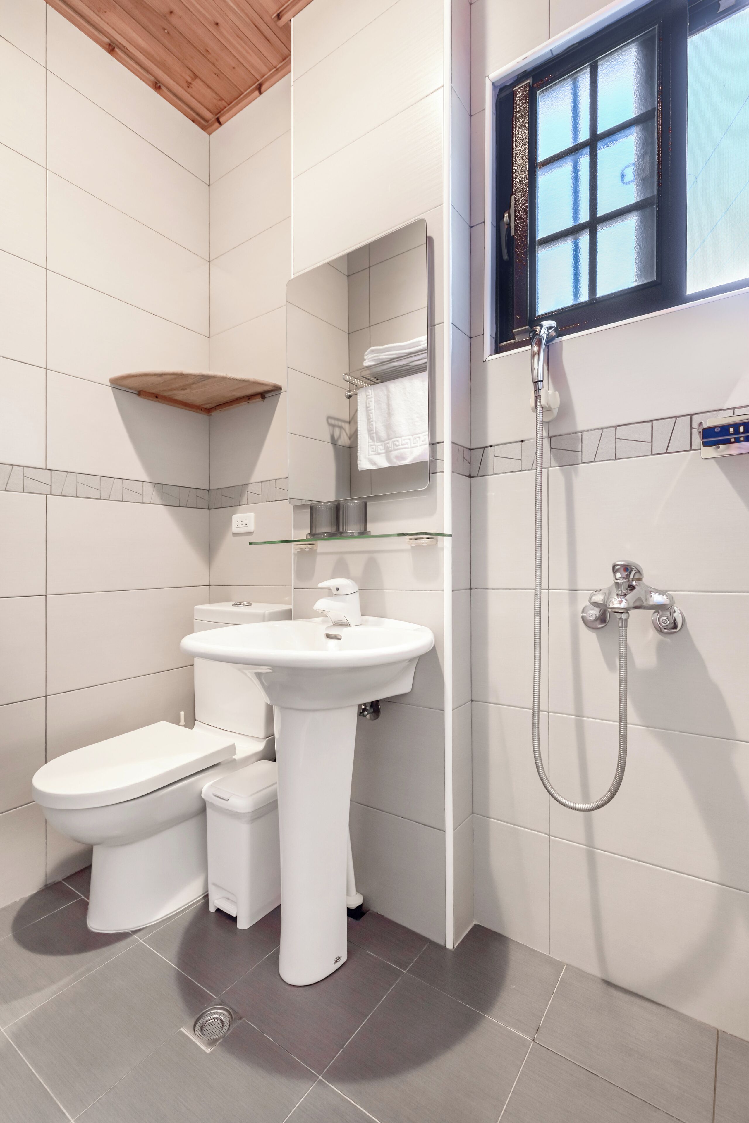 A modern bathroom with a white sink, toilet, and bidet, a glass shelf, and a shower with a control panel.
