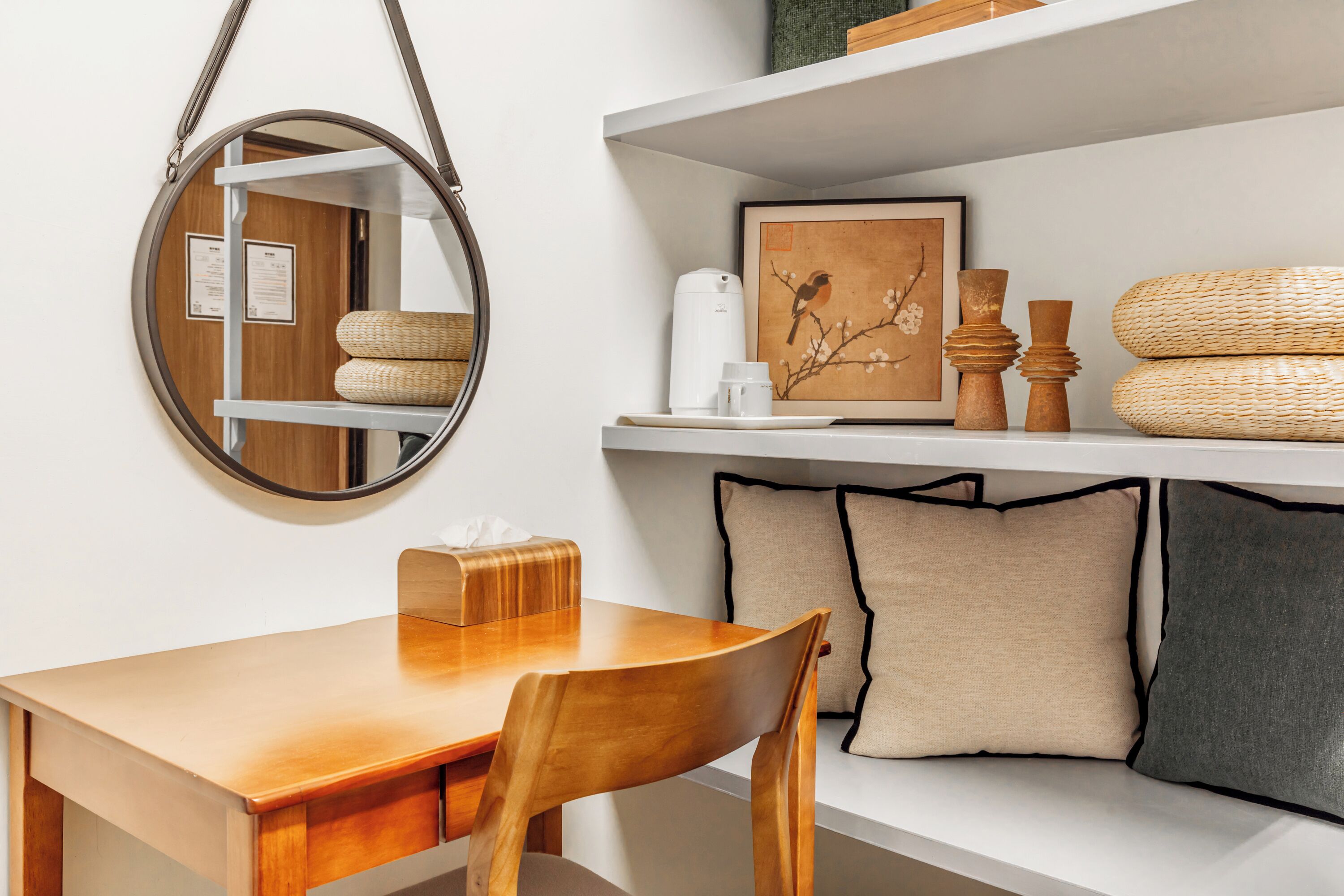 Una mesa de comedor de madera con un espejo encima, un estante blanco con adornos, y un cuadro en la pared.