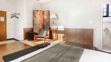 A modern hotel room with a bed, a wooden floor, a tatami mat, a traditional Japanese screen, a black and white chair, and a standing lamp.