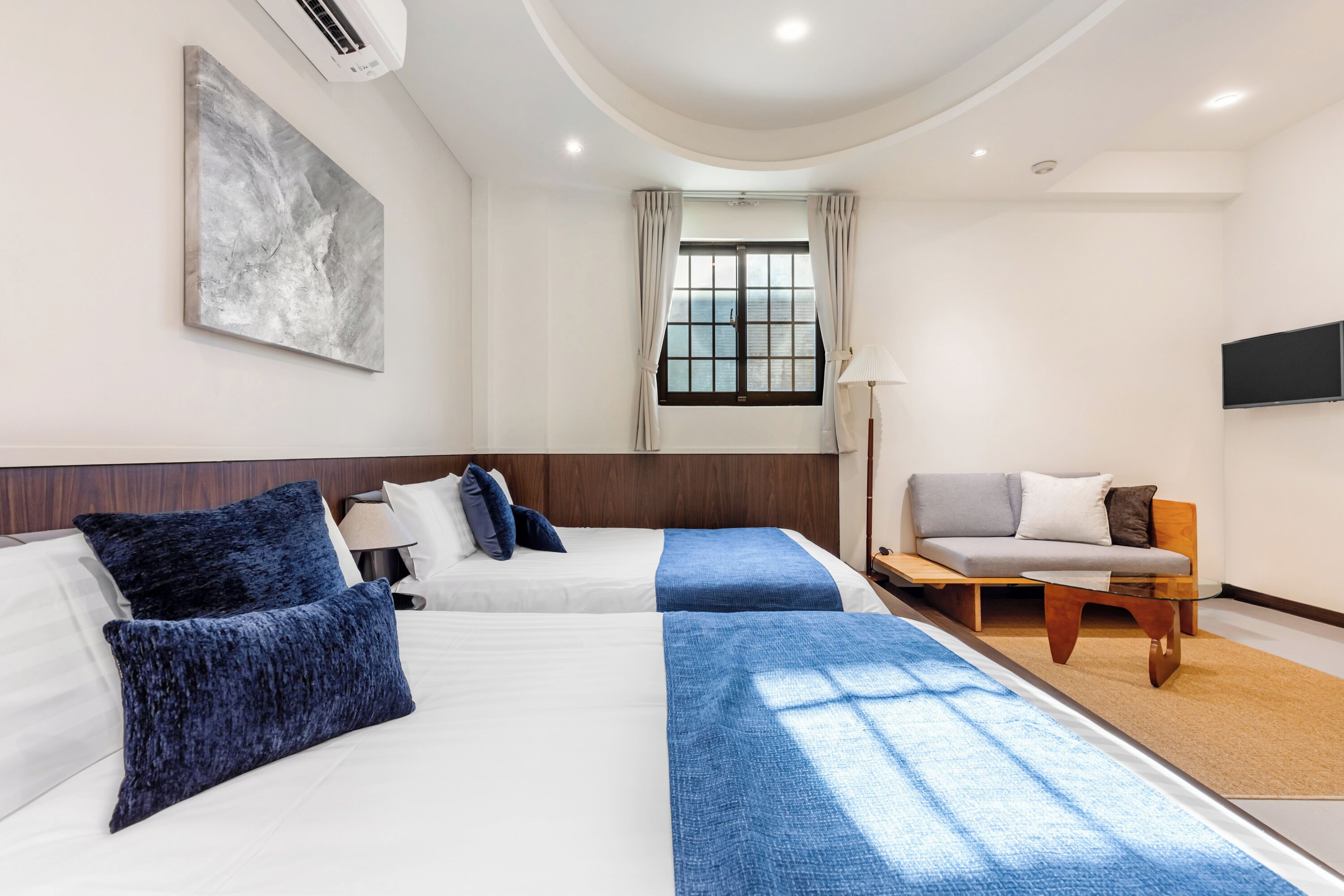 A hotel room with two beds, a sofa, a TV, and a window with curtains.