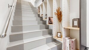 A staircase with alternating light and dark gray steps, metal handrails, and shelves with books and decorative items. - Harmony Easy Stay (New Taipei City)