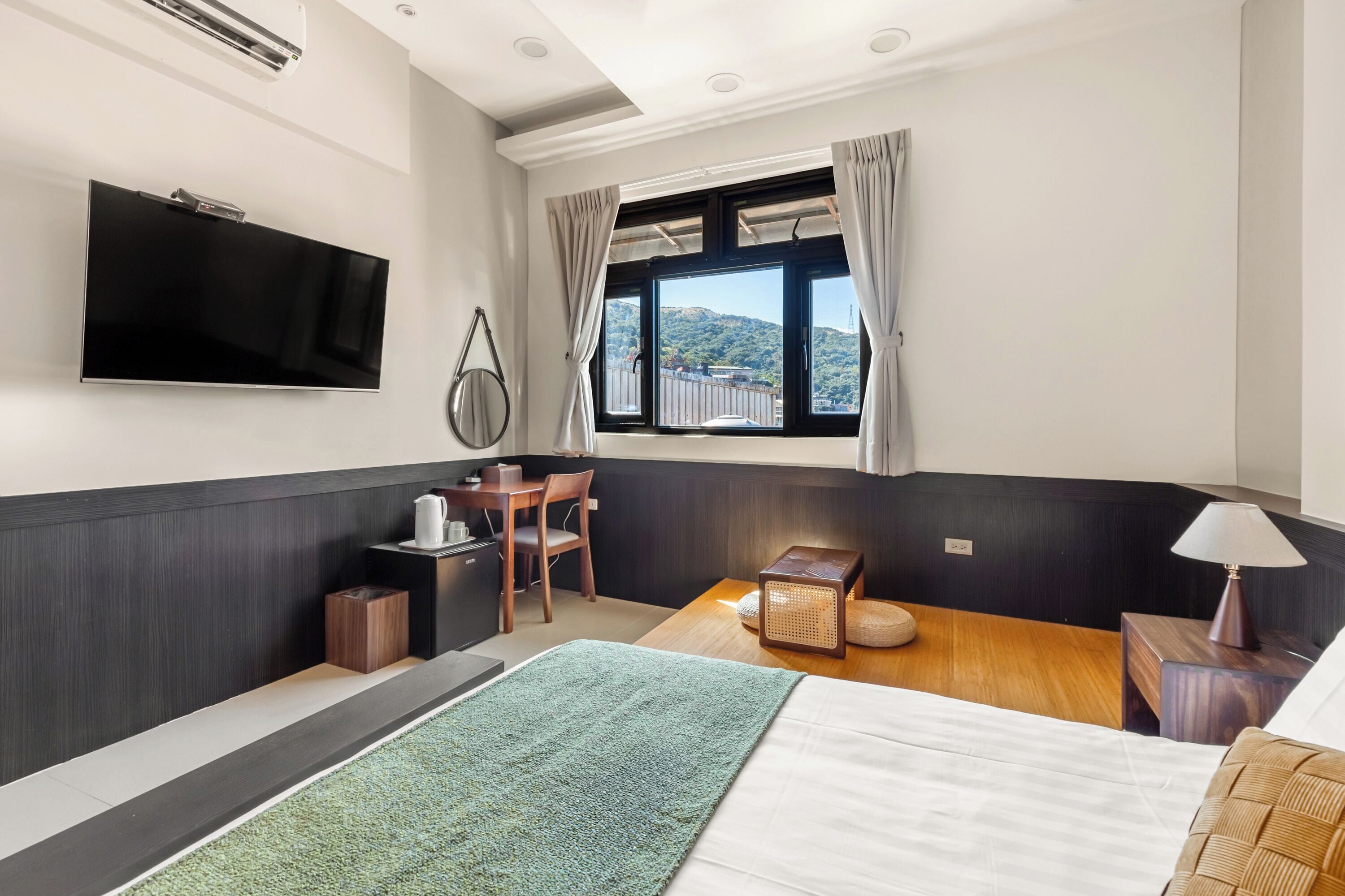 A modern hotel room with a bed, a desk, a television, and a window with curtains.