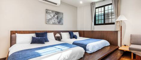 A hotel room with two beds, a large window with curtains, a wall-mounted air conditioner, and a painting.