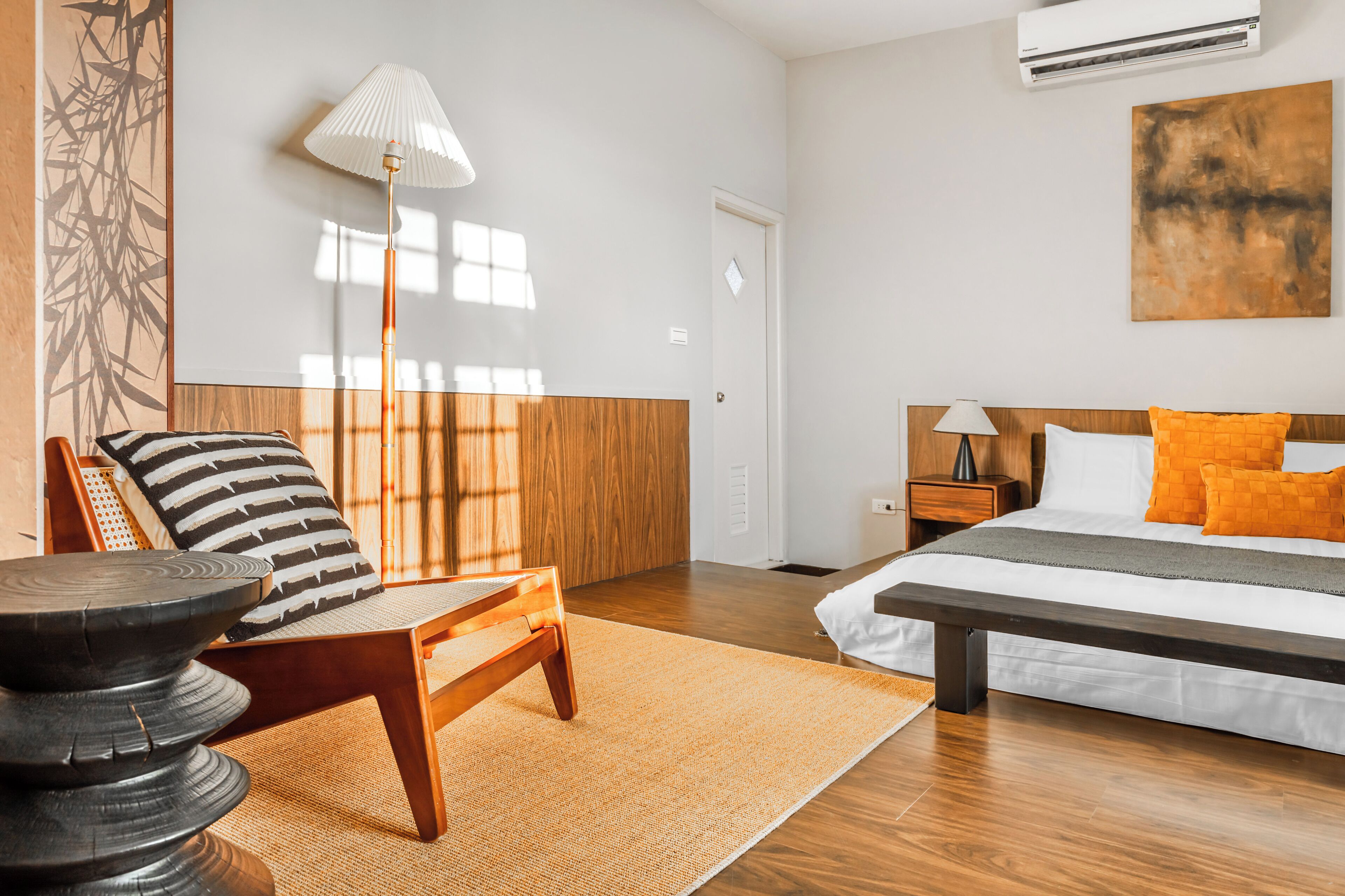 A hotel room with a bed, a chair, a lamp, and a wall art piece.