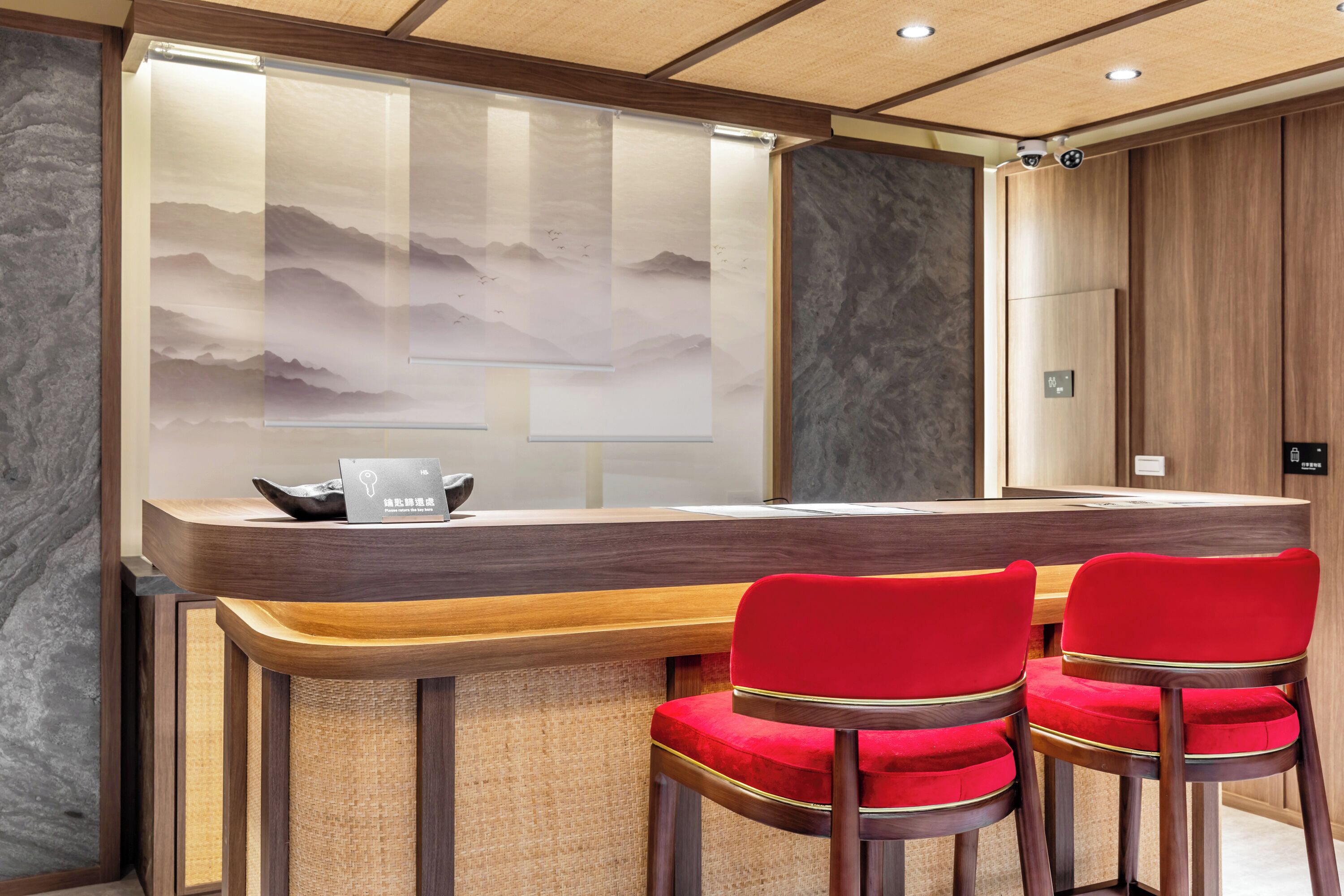 A reception desk with a wooden counter and two red upholstered chairs.