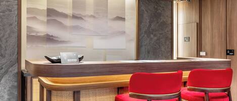 A reception desk with a wooden counter and two red upholstered chairs.
