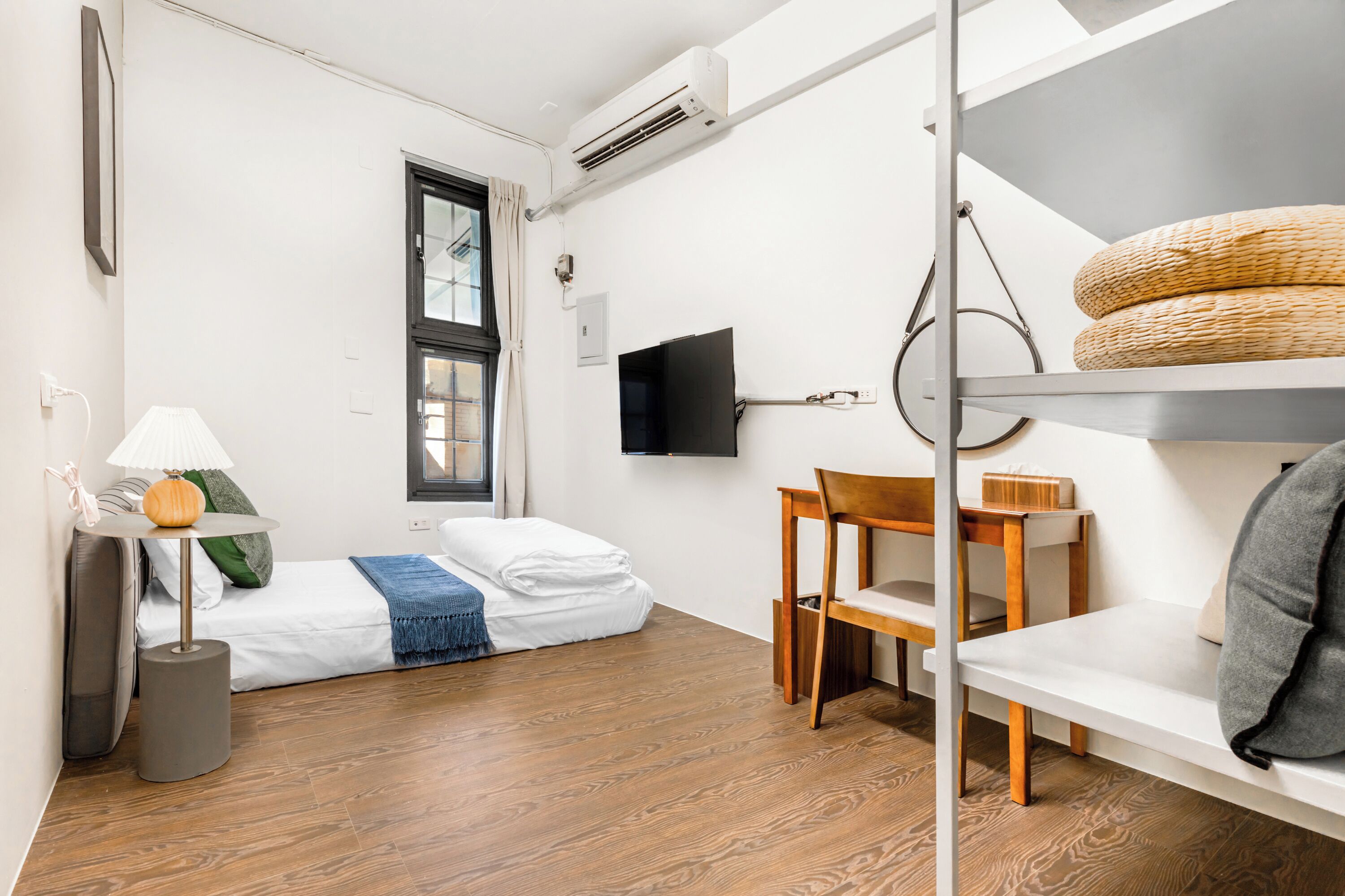 A compact room with a bed, a desk, a chair, a TV, and a shelf with baskets.