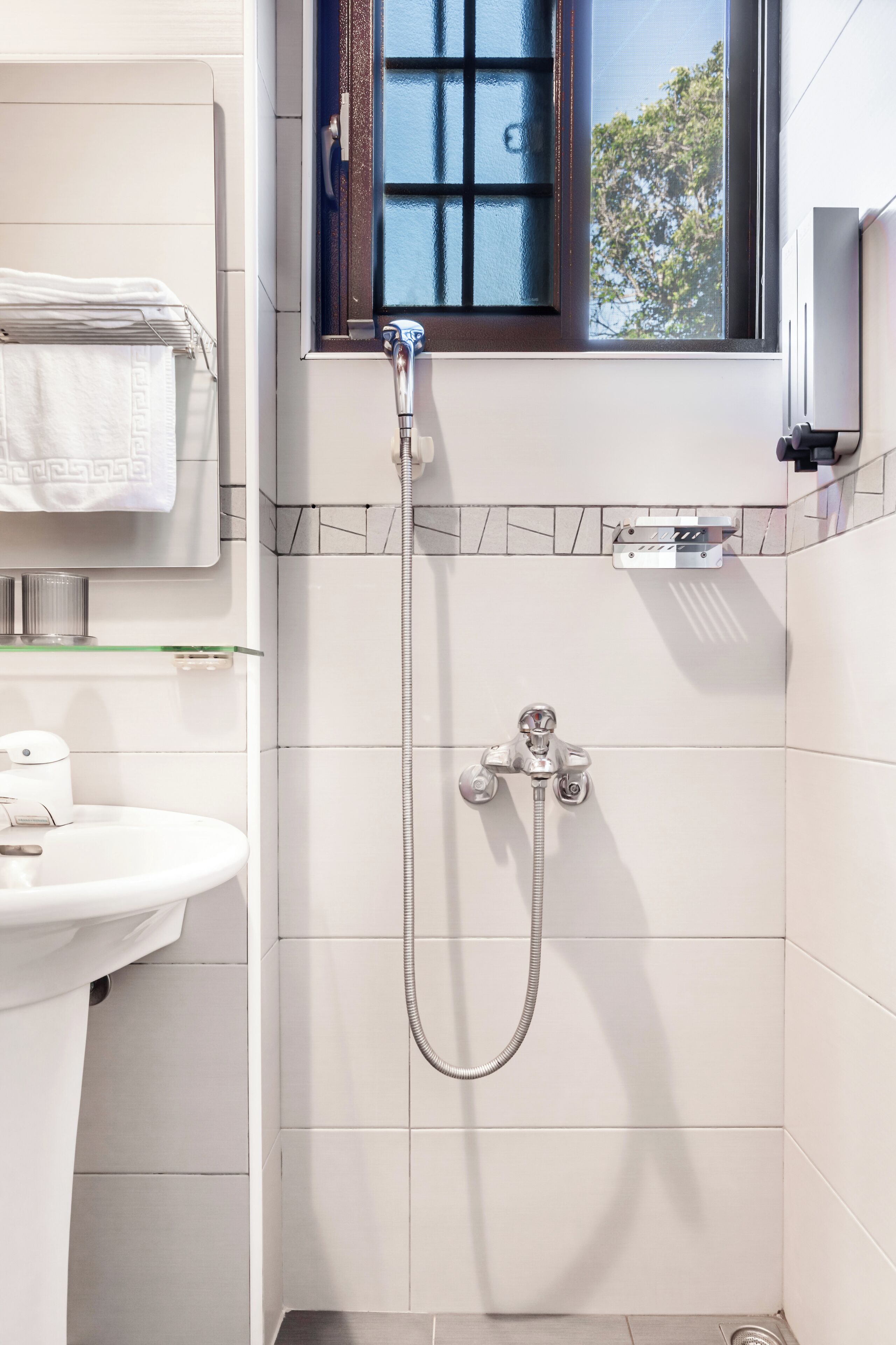 Une salle de bain avec une douche, un lavabo et une fenêtre donnant sur les arbres.