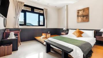 Ein modernes Hotelzimmer mit einem großen Bett, Nachttischen, einem Schreibtisch mit Stuhl, einem Fenster mit Vorhängen und Blick ins Freie.