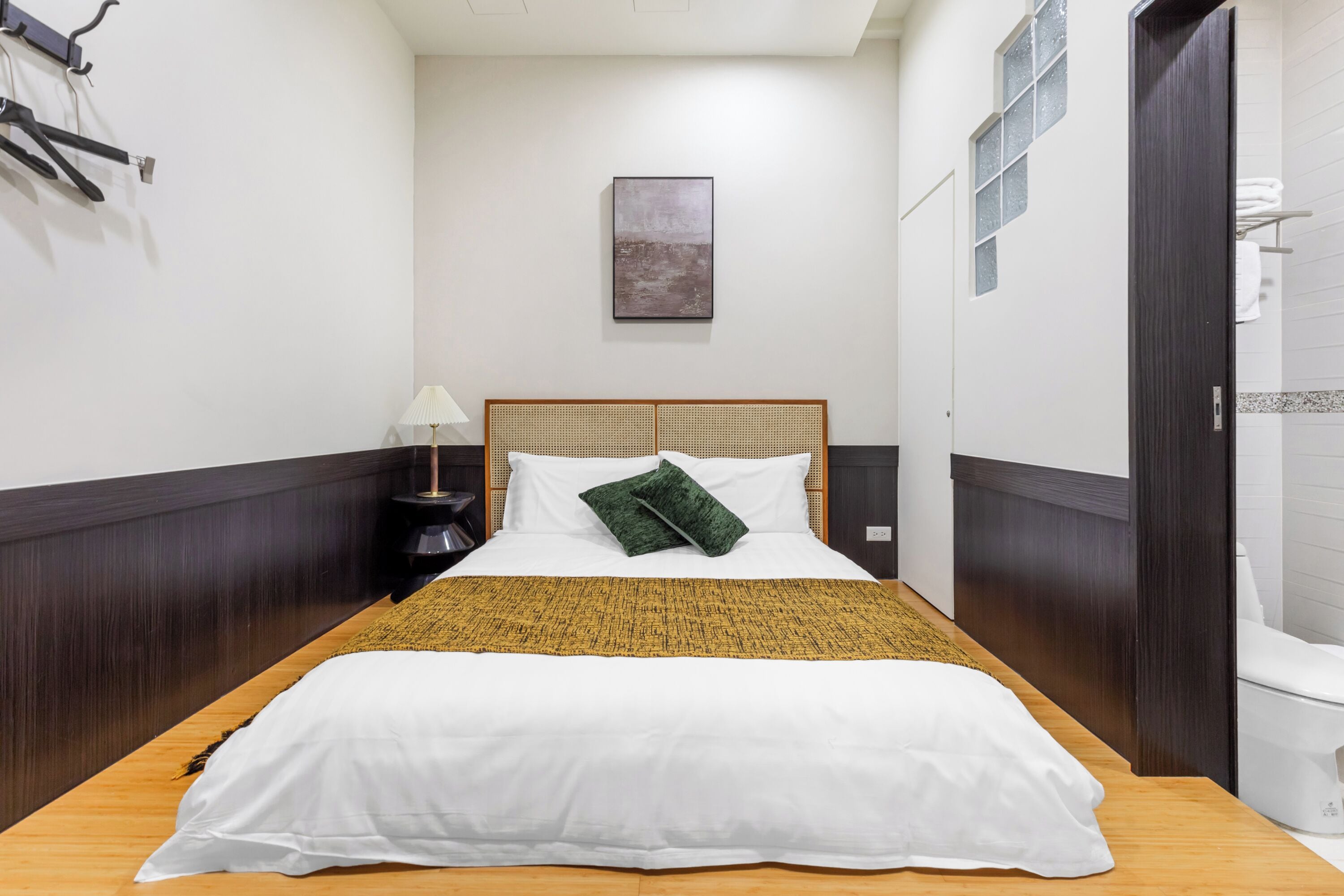 Un dormitorio ordenado con cama, mesita de noche, lámpara y un cuadro en la pared.